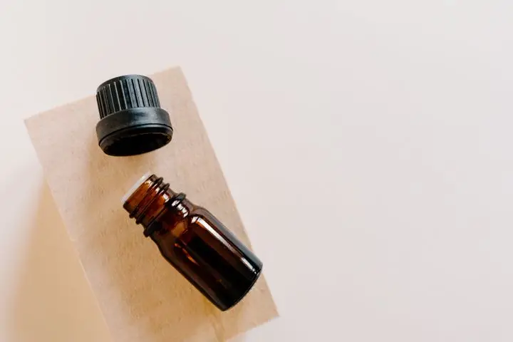 High-angle shot of an open brown essential oil bottle with its cap off on a wooden surface.