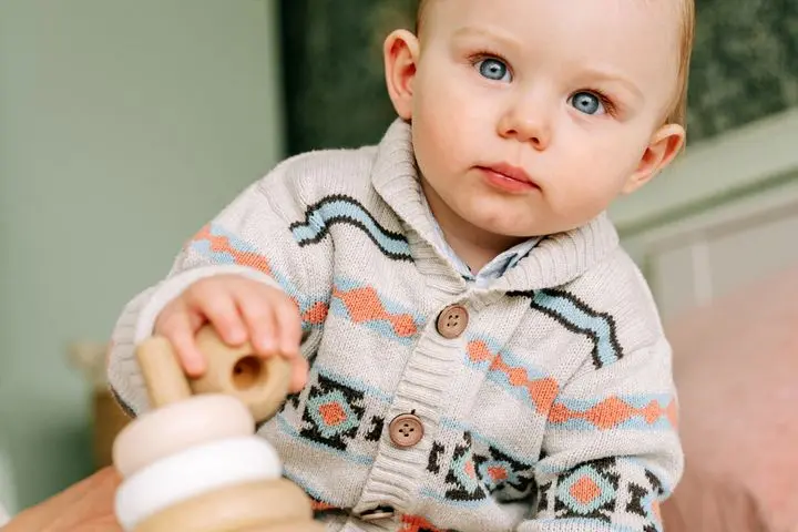 Adorable toddler wearing a cozy sweater, playing indoors with a wooden toy, showcasing innocence and curiosity.