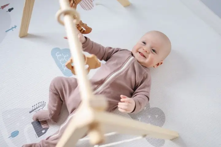 A joyful baby lying on a soft mat, playing with wooden toys, smiling brightly.