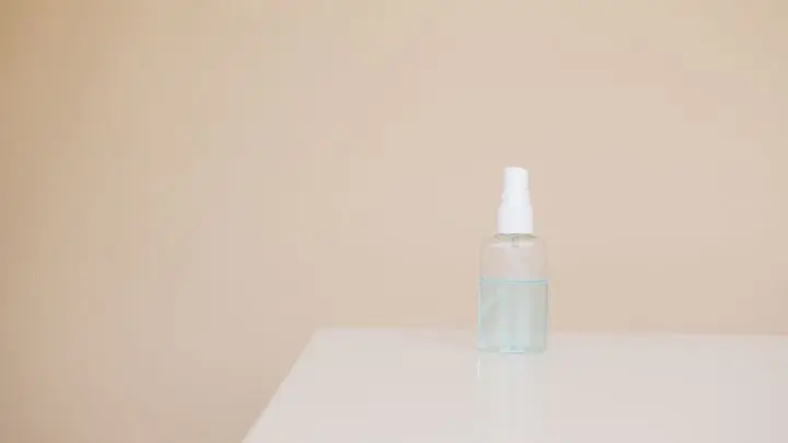 Small plastic bottle of hand antiseptic on white table near light brown wall