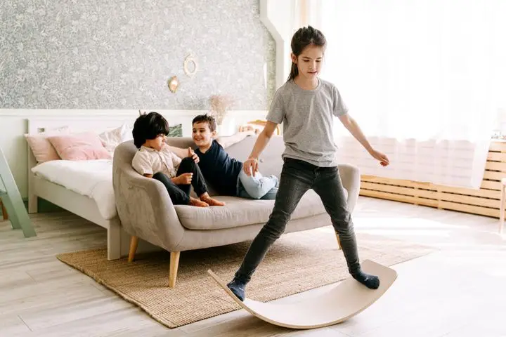 Three kids enjoying a balance board activity in a cozy bedroom setting.