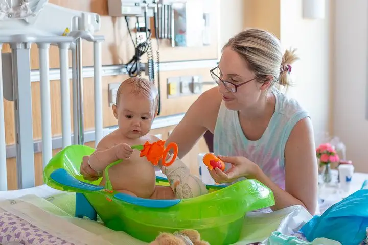 A mother lovingly bathes her baby in a hospital room, capturing a tender moment.
