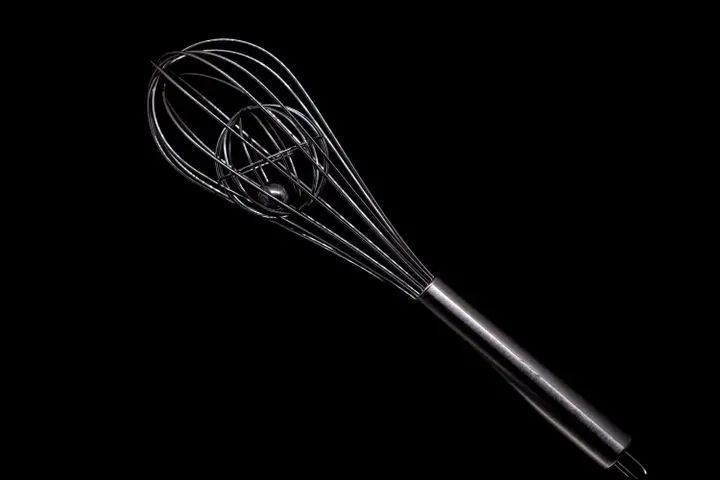 Elegant close-up of a stainless steel whisk against a black backdrop, showcasing its sleek design.