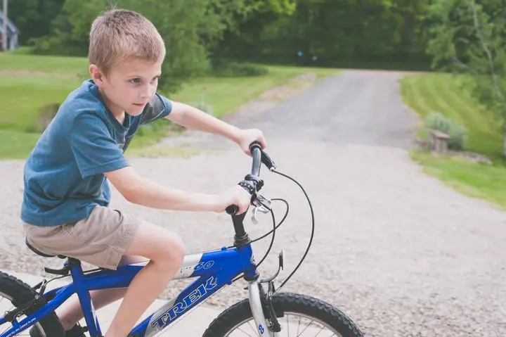 A young boy enjoying a bicycle ride on a sunny day along a gravel path surrounded by greenery.