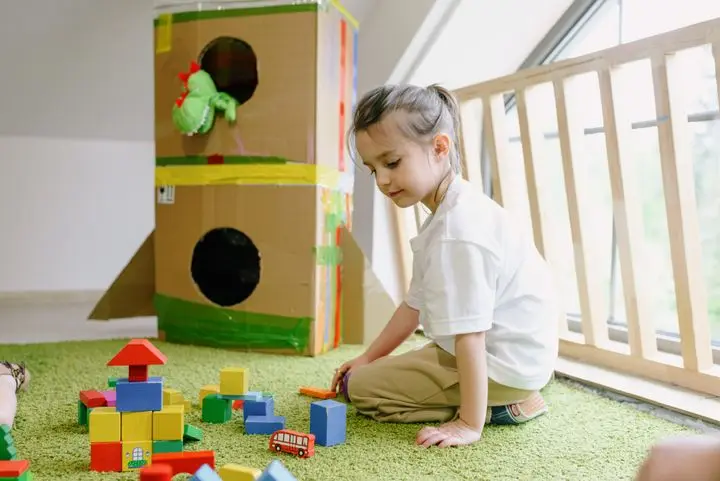 Young girl playing with colorful blocks in a bright indoor playroom.