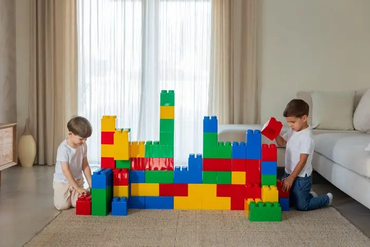 Two young boys enjoy building with large, colorful blocks in a bright indoor setting.