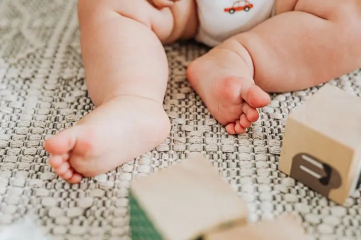 Close-up of baby feet on a rug surrounded by wooden toy blocks, conveying playfulness and innocence.