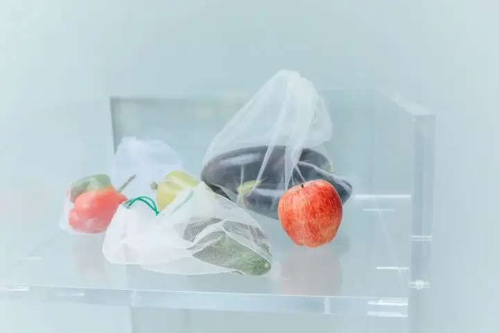 Reusable produce bags filled with fresh vegetables and a red apple, promoting eco-friendly shopping.