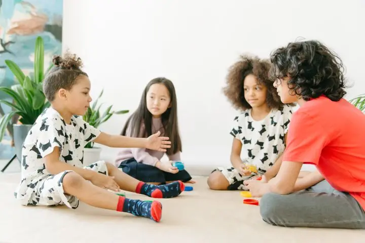 A group of four children sitting on the floor, engaging and playing together indoors.