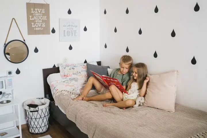 Two children reading a book together on bed in a cozy and playful bedroom setting.