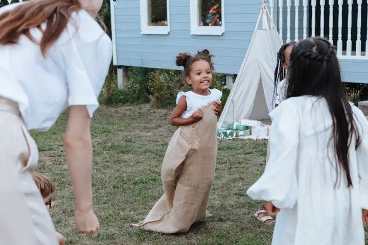 Children enjoying a fun sack race outdoors amid party vibes and cheerful laughter.
