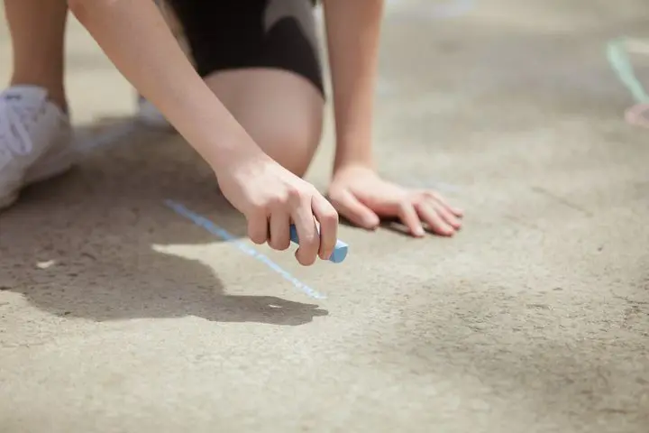 Young person drawing on outdoor pavement with colorful chalk.