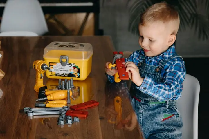 A young boy enjoying playtime with colorful toy tools on a wooden table indoors.