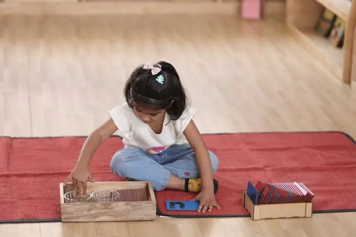 Young girl explores Montessori materials inside a classroom.