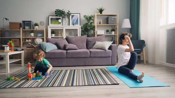 A mother practicing yoga and her child playing with blocks in a cozy living room.