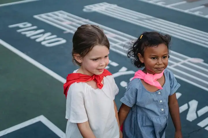 Two young girls in colorful scarves playing and smiling on a playground.