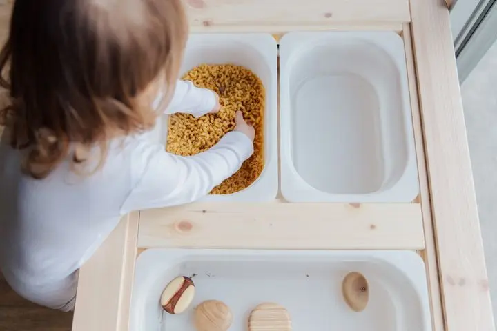 Curious child engaging in sensory play with pasta, exploring textures indoors.