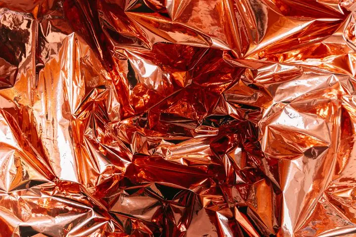 Crumpled metallic foil with a shiny orange texture, creating an abstract background.