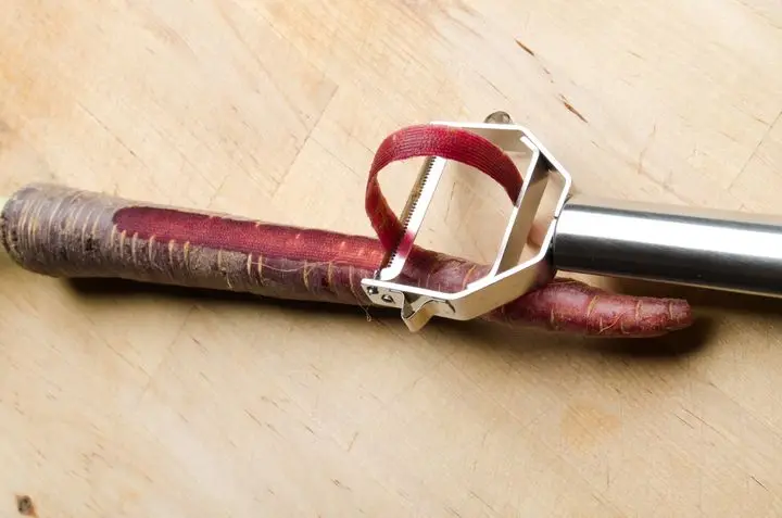 An innovative vegetable peeler peeling a purple carrot on a wooden surface.