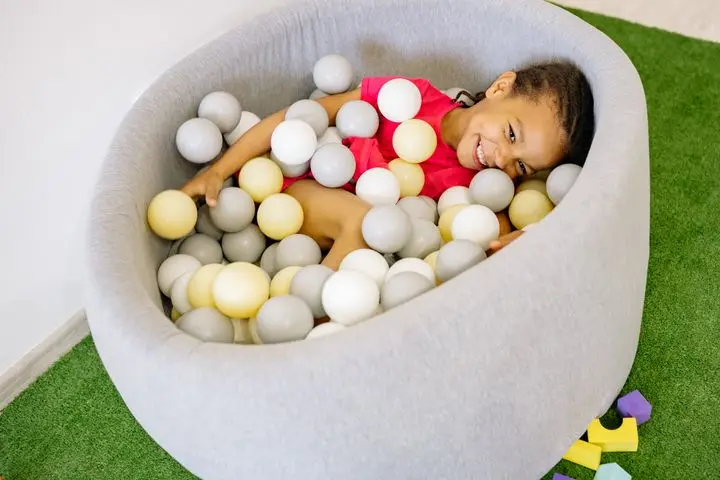 Smiling child enjoying playtime in a colorful indoor ball pit at a nursery.