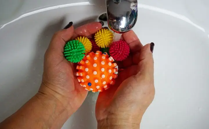 Hands holding colorful rubber balls under running water in a sink, perfect for toy washing themes.