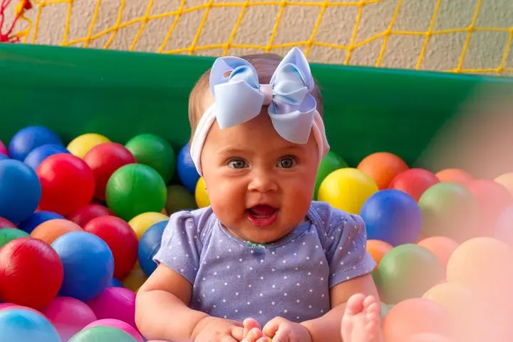Charming baby with blue bow smiling amidst vibrant plastic balls. Perfect for childhood themes.