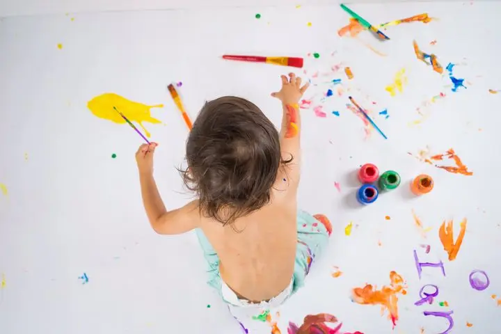 A child artist expressing creativity with vivid colors on a large canvas using finger paints.