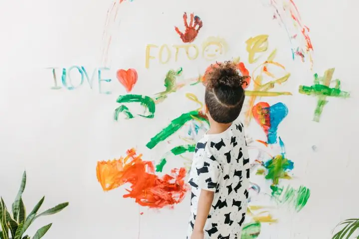 A child engages in creative art on a white wall with vibrant colors indoors.