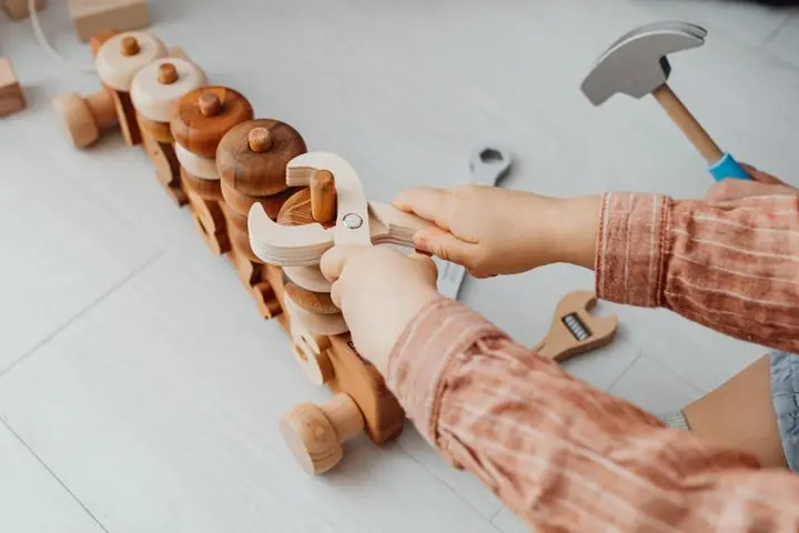 A young child using toy tools to play with a wooden train indoors. Creative playtime.