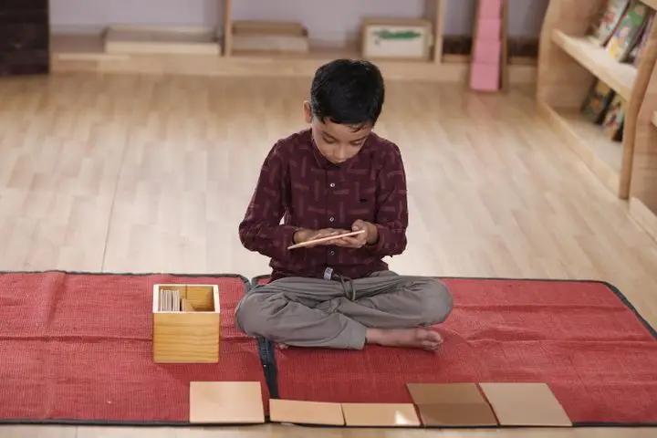 A child immersed in Montessori floor activity with learning cards on a red mat indoors.