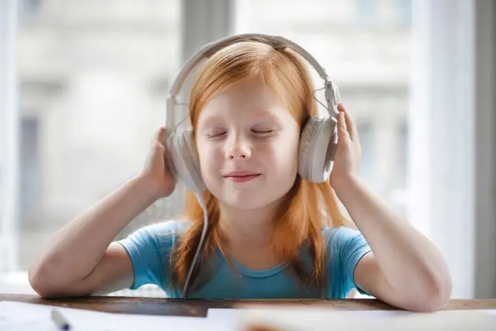 A young girl with headphones enjoying music indoors with a joyful expression.