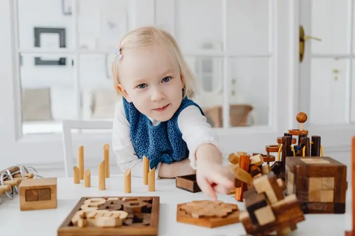 Blonde girl enjoying a creative moment with educational wooden toys indoors.