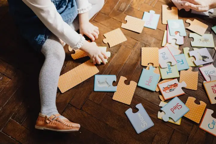 Child engaging with educational puzzle pieces on wooden floor indoors, fostering learning and play.