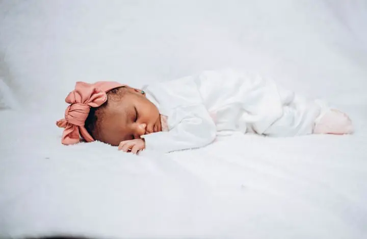 Adorable baby sleeping peacefully on white fabric, wearing a pink headband.