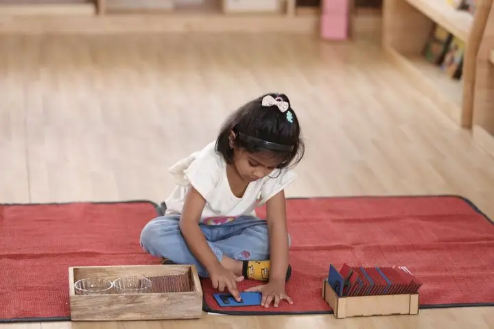 A young girl is focused on a Montessori learning activity with cards, fostering early childhood education.