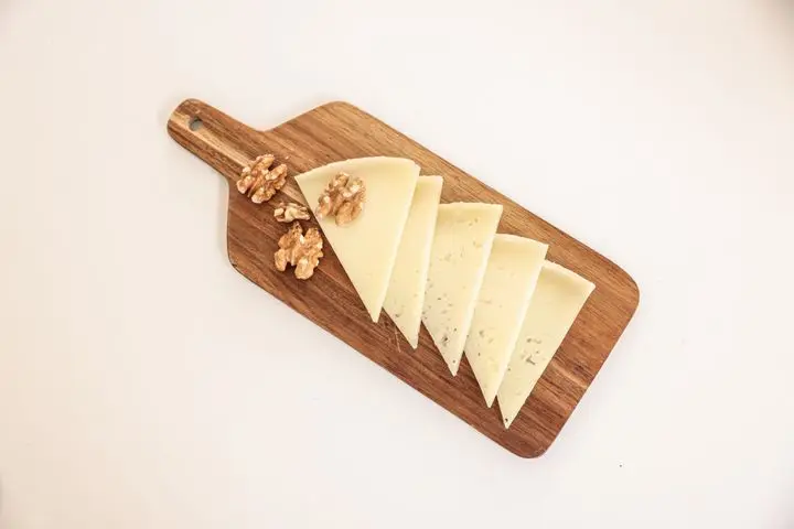 Top view of sliced cheese and walnuts on a wooden cutting board against a white background.