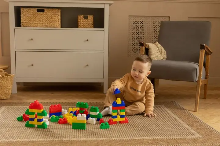 A young boy playing with colorful building blocks on a rug in a cozy room.