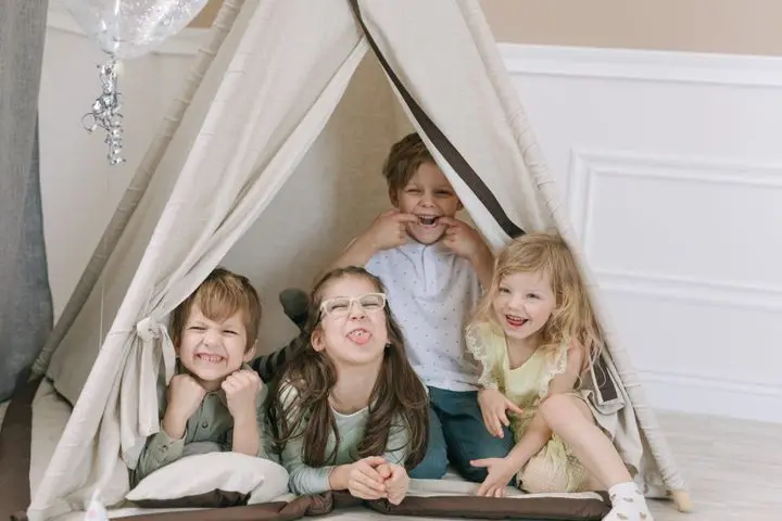 Four cheerful kids making faces inside a cozy indoor play tent, smiling and having fun.