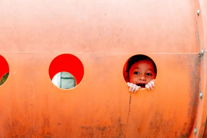A joyful child peeks through a playground tunnel in Mexico City, capturing the essence of playful childhood.