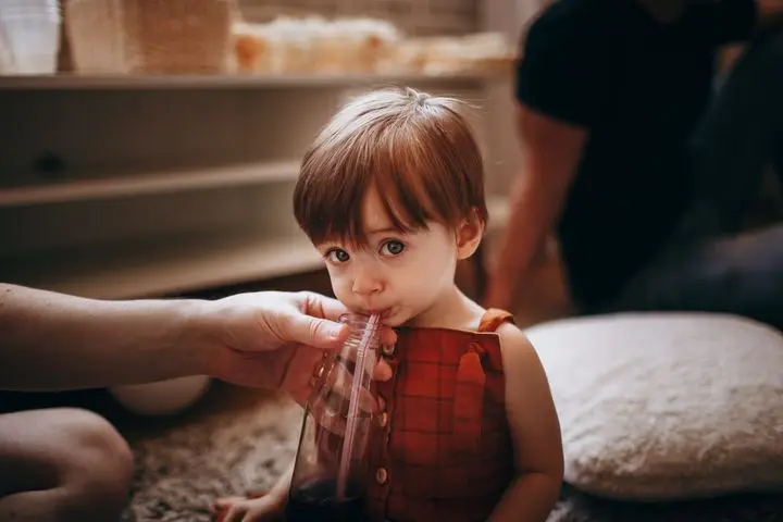 Cute child drinking with a straw indoors, capturing a tender moment with warm lighting.