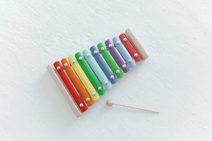 Brightly colored xylophone with wooden mallet on a white surface, showcasing vibrant musical tones.