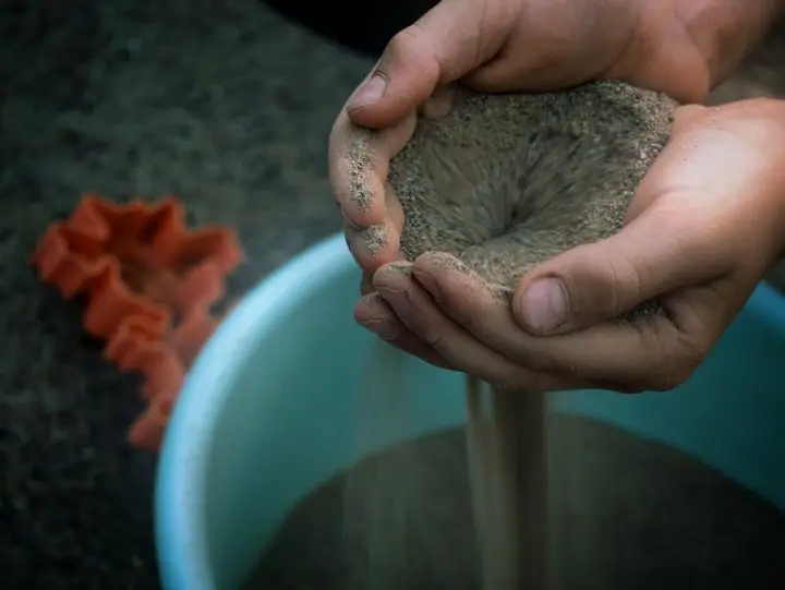 Hands gently sifting sand through fingers with scattered molds nearby, creating a playful scene.
